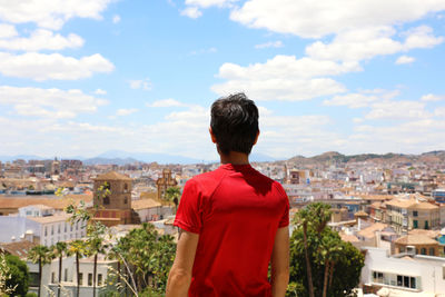 Rear view of man looking at cityscape against sky