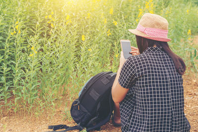 Rear view of woman using smart phone while sitting on field