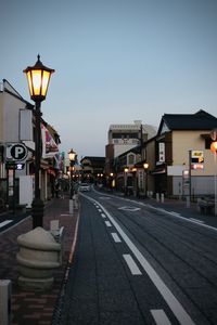 Illuminated street lights by buildings against sky at dusk