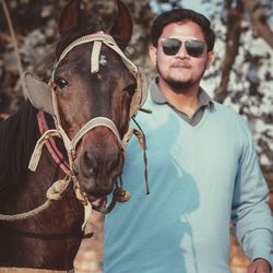 Portrait of man wearing sunglasses standing by horse outdoors