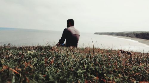 Rear view of man sitting on cliff in front of sea