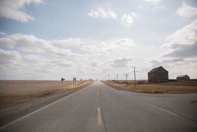 Empty road amidst field against sky