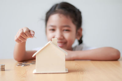 Close-up of smiling girl with coins and model home on table