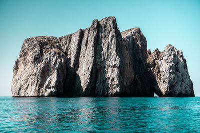 Rock formation by sea against clear blue sky