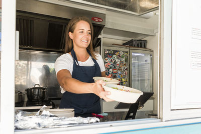 Smiling young female owner giving bowls while standing in food truck