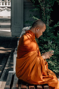 Monk using mobile phone while sitting on seat