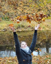 Portrait of smiling young woman with autumn leaves in water