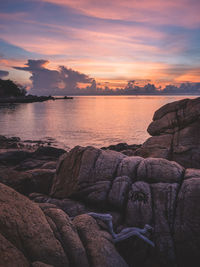 Scenic view of sea against orange sky during sunrise with textured rocky beach. koh samui, thailand.