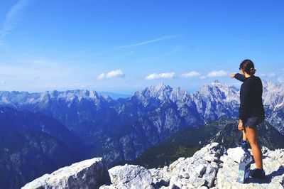 Rear view of young woman pointing while on mountain against sky