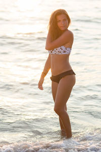 Portrait beautiful woman with hand in hair standing by sea during sunset