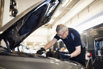 Senior mechanic holding mobile phone while repairing car at shop