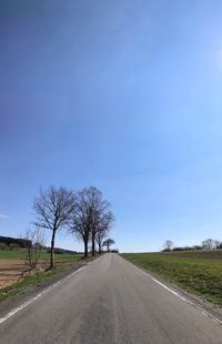 Road amidst trees on field against sky