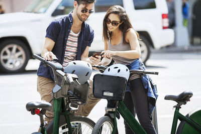 Couple using smart phone while standing with bicycles on street