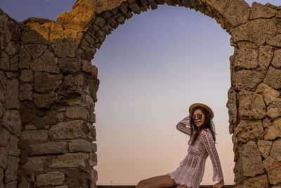 Portrait of young woman wearing hat standing against sky