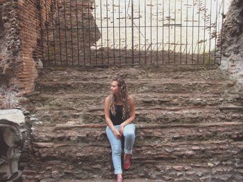 Full length of young woman sitting on steps against gate