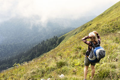 Young woman with backpack wearing cap hiking in green mountains in summer healthy active lifestyle