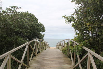 Wooden footbridge leading to sea against sky