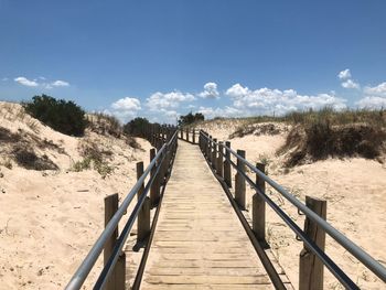 Wooden railing on steps by trees against sky