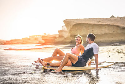 Couple sitting on surfboard at shore of beach