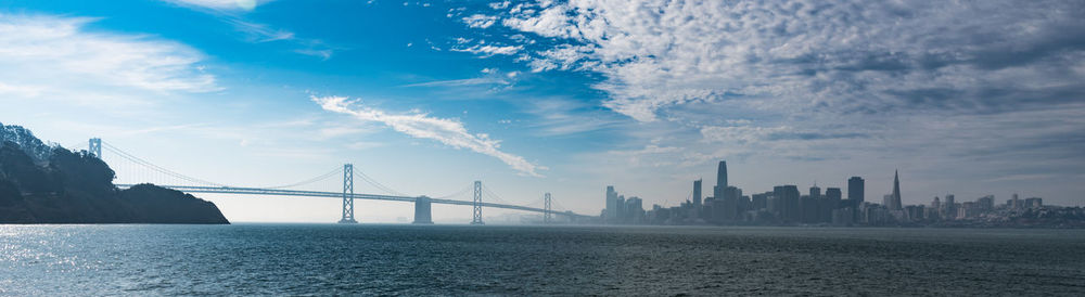 Suspension bridge over river against cloudy sky