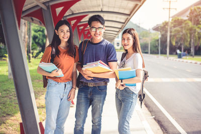 Portrait of friends with books standing on footpath