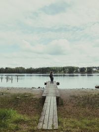 People sitting on pier over lake against sky