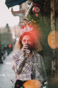 Young woman drinking hot coffee from a takeaway cup while standing against trees