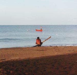 Rear view of man sitting at beach against sky