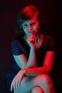 Portrait of smiling woman sitting against black background