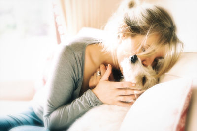 Young woman kissing dog while sitting on sofa at home