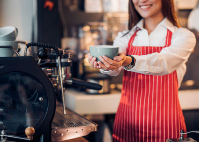 Midsection of smiling barista holding coffee cup in cafe