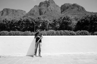 Young man standing by retaining wall against mountains
