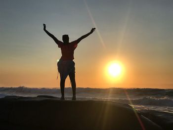 Rear view of man standing at seaside during sunset