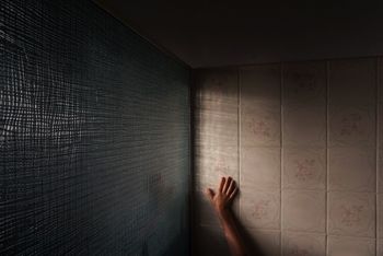 Cropped hand of man touching tiled wall in bathroom