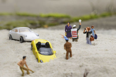 Figurines and toy cars on sand at beach