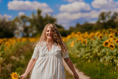 Portrait of smiling young woman standing by flowering plants on field