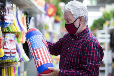 Senior man wearing mask holding punching bag at store