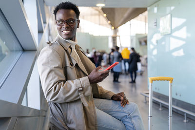 Smiling young man using mobile phone looking away while sitting at airport