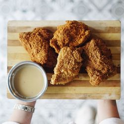 Cropped hands of woman holding fried chicken with dip on cutting board