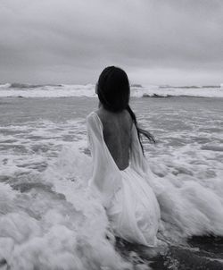 Rear view of woman at beach against sky