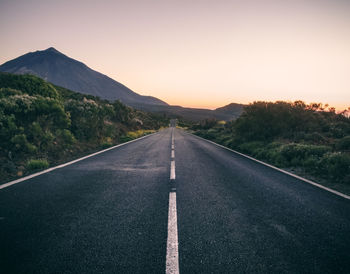 Empty road leading towards mountains against clear sky