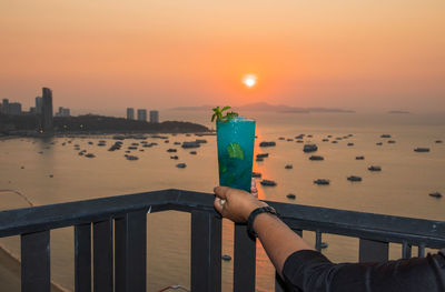 Person holding umbrella against sea during sunset