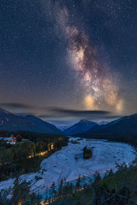 Scenic view of landscape and snowcapped mountains against star field in sky at night