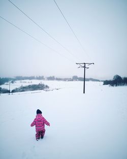 Rear view of a kid standing by snow against sky