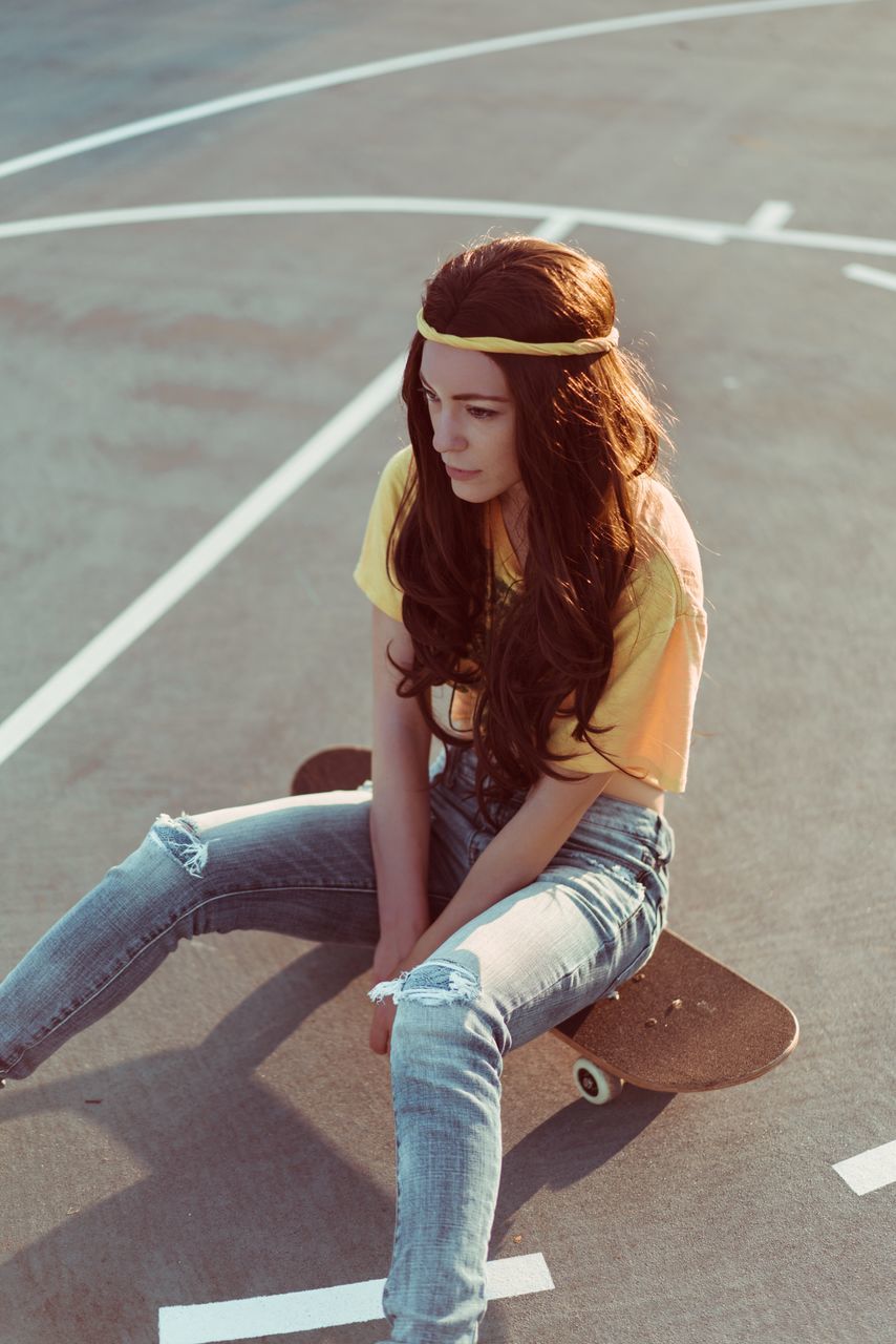 casual clothing, one person, leisure activity, young adult, smiling, young women, jeans, happiness, real people, skateboard, day, lifestyles, outdoors, sunlight, beautiful woman, portrait, looking at camera, full length, road, sitting, people