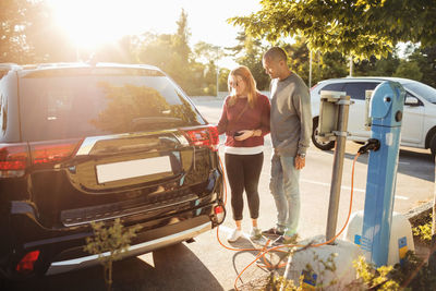 Mature couple charging electric car at station on sunny day