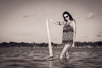 Portrait of young woman standing by lake against sky