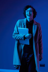 Portrait of young woman standing against blue background