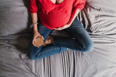 Midsection of pregnant woman with tea sitting on bed at home