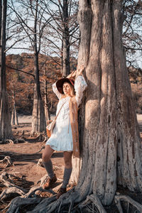 Full length of woman standing by tree trunk in forest